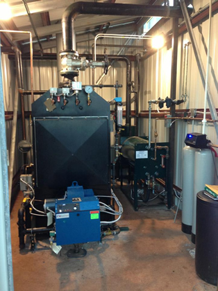 MPH 100 low pressure steam boiler with burner (blue). Water treatment system at right and horizontal feed tank at right rear.